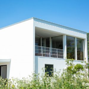 ２階テラスが特徴の白い外観の住まいと自然の緑