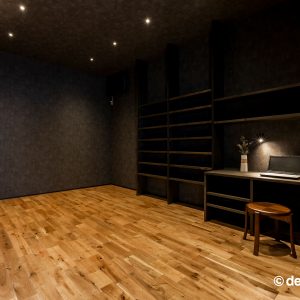 壁・天井のブラックのクロスと木のフローリングを組み合わせた造作の収納棚・カウンターのある書斎