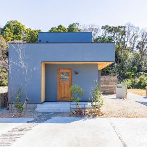 ネイビーの塗り壁に、木目の玄関ドアと軒天が映える住宅の外観